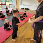 A young boy in a martial arts uniform receives a new grade belt at the front of his class