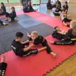 Children in martial arts suits do stretching in pairs on a gym mat
